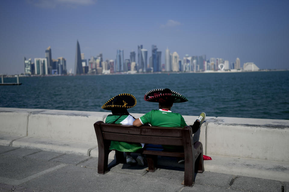 Dos aficionados mexicanos, tocados con el tradicional sombrero charro, sentados en un banco en el paseo marítimo de Doha, el 21 de noviembre de 2022. (AP Foto/Natacha Pisarenko)