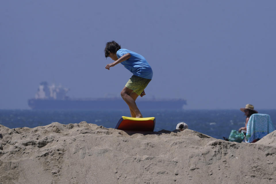 A boy slides with a surf board on top of a sand berm in Seal Beach, Calif., Friday, Aug. 18, 2023. Officials in Southern California were also re-enforcing sand berms, built to protect low-lying coastal communities against winter surf. Hurricane Hilary is churning off Mexico's Pacific coast as a powerful Category 4 storm threatening to unleash torrential rains on the mudslide-prone border city of Tijuana before heading into Southern California as the first tropical storm there in 84 years. (AP Photo/Damian Dovarganes)