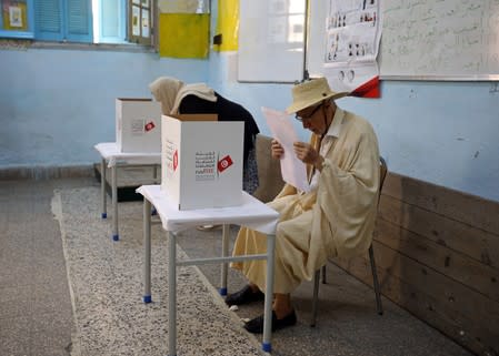 Man reads his ballot paper at a polling station during presidential election in Tunis