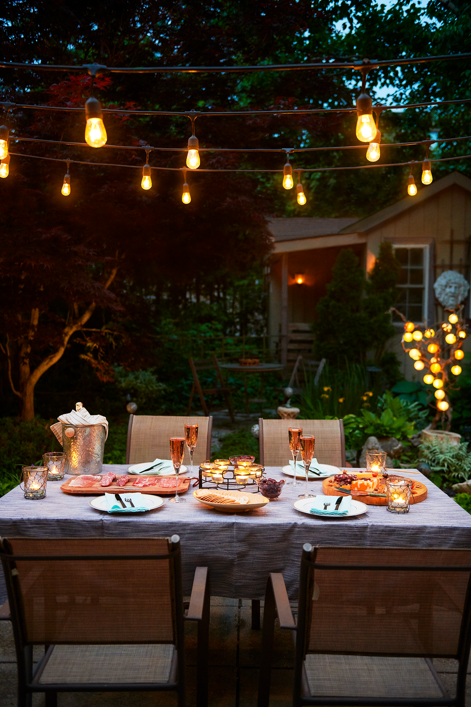patio lights turned on at outdoor evening patio dinner party with pink champagne, charcuterie board and cheese platter