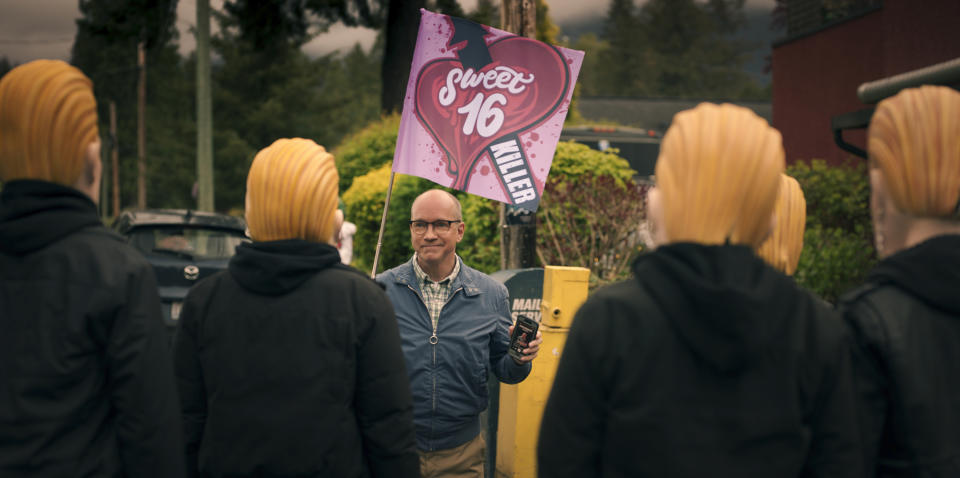 Man in present day holding Sweet 16 sign surrounded by masked people.