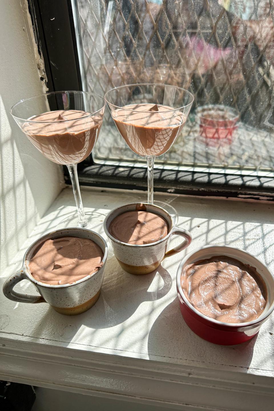Three servings of chocolate mousse in varying containers on a windowsill