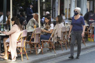 A woman wears a mask as she passes people dinning out in London, Monday, Sept. 21, 2020. Britain's top medical advisers have painted a grim picture of exponential growth in illness and death if nothing is done to control the second wave of coronavirus infections, laying the groundwork for the government to announce new restrictions later this week. (AP Photo/Kirsty Wigglesworth)