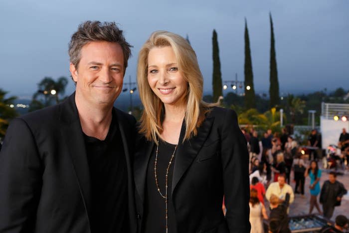 Matthew Perry and Lisa Kudrow smiling at an outdoor event with people in the background