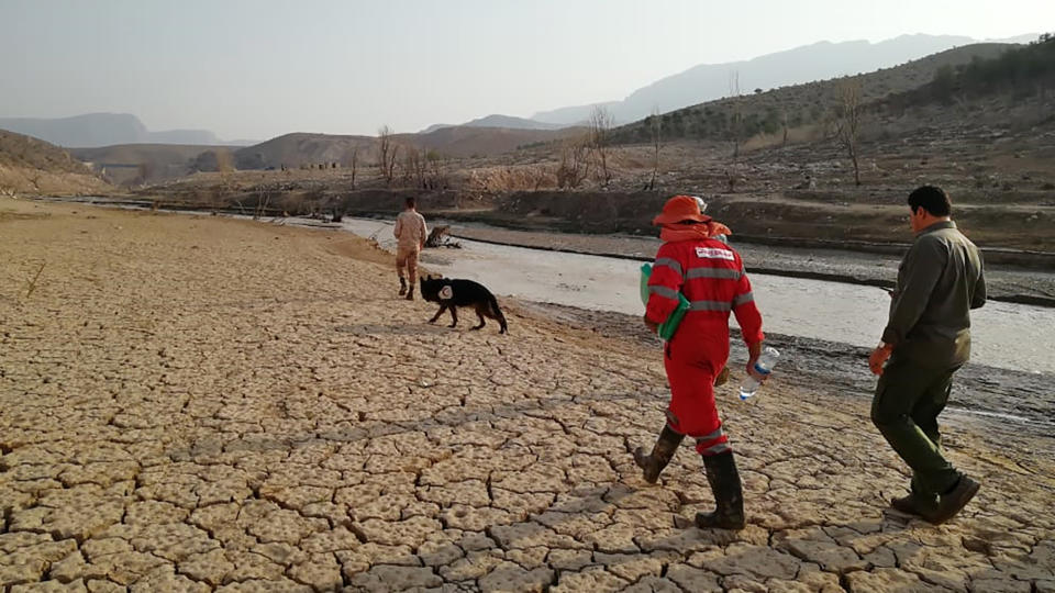 In this photo provided by the Iranian Red Crescent Society on Saturday, July 23, 2022, members of a rescue team search for missing people of Friday's flash floods in Iran's drought-stricken southern Fars province, Iran. Heavy rains swelled the Roudbal river by the city of Estahban, according to the city's governor Yousef Karegar. (Iranian Red Crescent Society via AP)