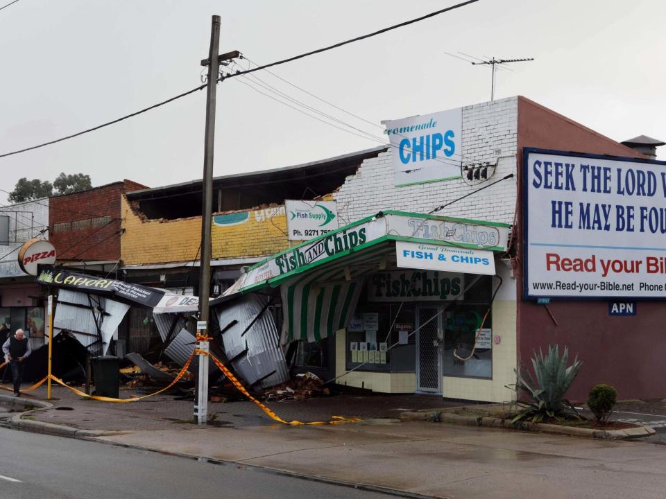 A man (L) walks past shops roped off after they sustained damage in the Perth suburb of Bedford after the area was lashed by gale force winds and a tidal surge from the remnants of Tropical Cyclone Mangga: AFP via Getty Images