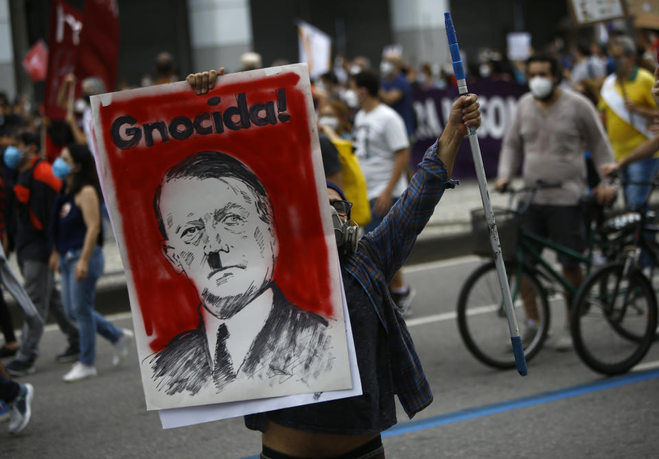 A protester holds a poster depicting Brazilian President Jair Bolsonaro as Adolf Hitler and the Portuguese word for genocidal, during a demonstration against Bolsonaro's handling of the coronavirus pandemic and economic policies protesters say harm the interests of the poor and working class, in Rio de Janeiro, Brazil, Saturday, June 19, 2021. Brazil is approaching an official COVID-19 death toll of 500,000 — second-highest in the world. (AP Photo/Bruna Prado)