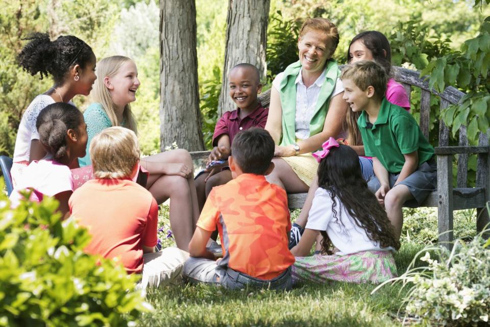 a group of kids and an adult in the woods chatting and laughing