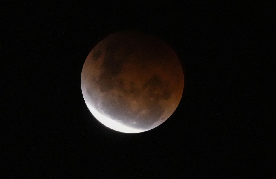 The Earth's shadow falls across the full moon above Sydney, Australia, Wednesday, May 26, 2021. The total lunar eclipse, also known as a super blood moon is the first in two years with the reddish-orange color the result of all the sunrises and sunsets in Earth's atmosphere projected onto the surface of the eclipsed moon. (AP Photo/Mark Baker)