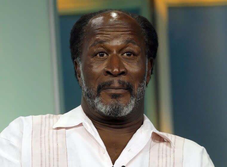 John Amos stares ahead in a white, striped shirt.