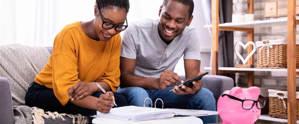 Young African Couple Sitting On Sofa Calculating Invoice