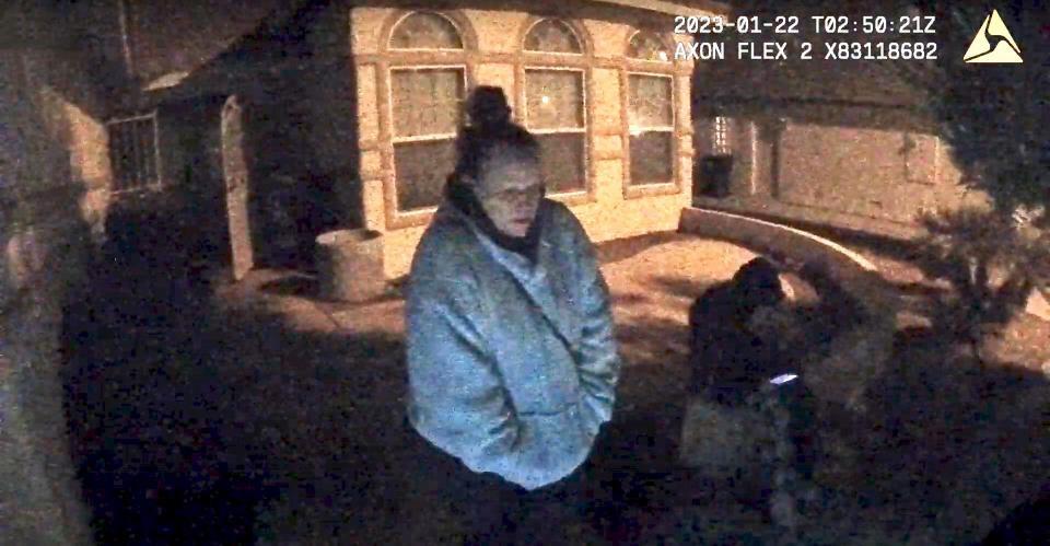 Blurry body cam footage of a woman in a blue sweatshirt standing outside her home in the dark next to a child in a black hoodie.