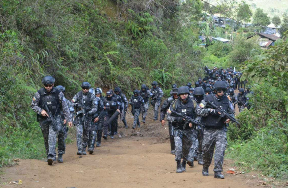 This photo released by Ecuador's National Police shows armed police arriving to raid an illegal gold mine in Buenos Aires, Ecuador, Tuesday, July 2, 2019. Independent miners have flocked to this area since gold was discovered in late 2017, before organized crime groups moved in to take control and, according to police, expand their list of crimes, including homicide to extortion to trafficking in people. (Ecuador National Police via AP)