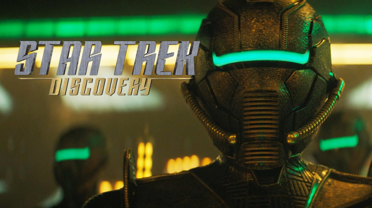  Promo image for the show "star trek: discovery," showing a closeup of a bronze-colored space helmet with a green line where eye slits would be. 