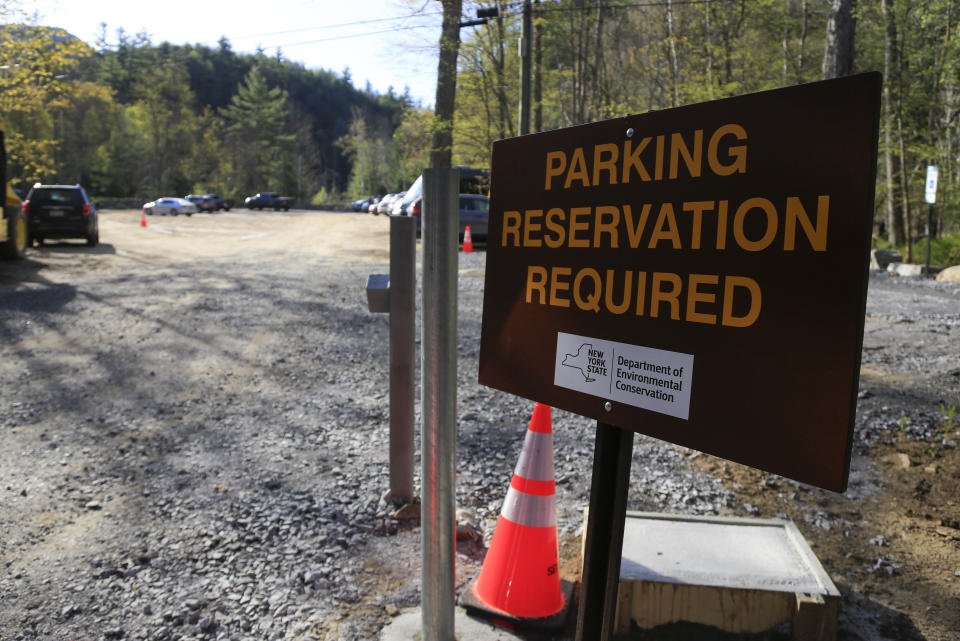 A parking reservation sign alerts visitors at the entrance to the Adirondack Mountain Reserve trailhead, Saturday, May 15, 2021, in St. Huberts, N.Y. A free reservation system went online recently to control growing numbers of visitors packing the parking lot and tramping on the trails through the private land of the Adirondack Mountain Reserve. The increasingly common requirements, in effect from Maui to Maine, offer a trade-off to visitors, sacrificing spontaneity and ease of access for benefits like guaranteed parking spots and more elbow room in the woods. (AP Photo/Julie Jacobson)