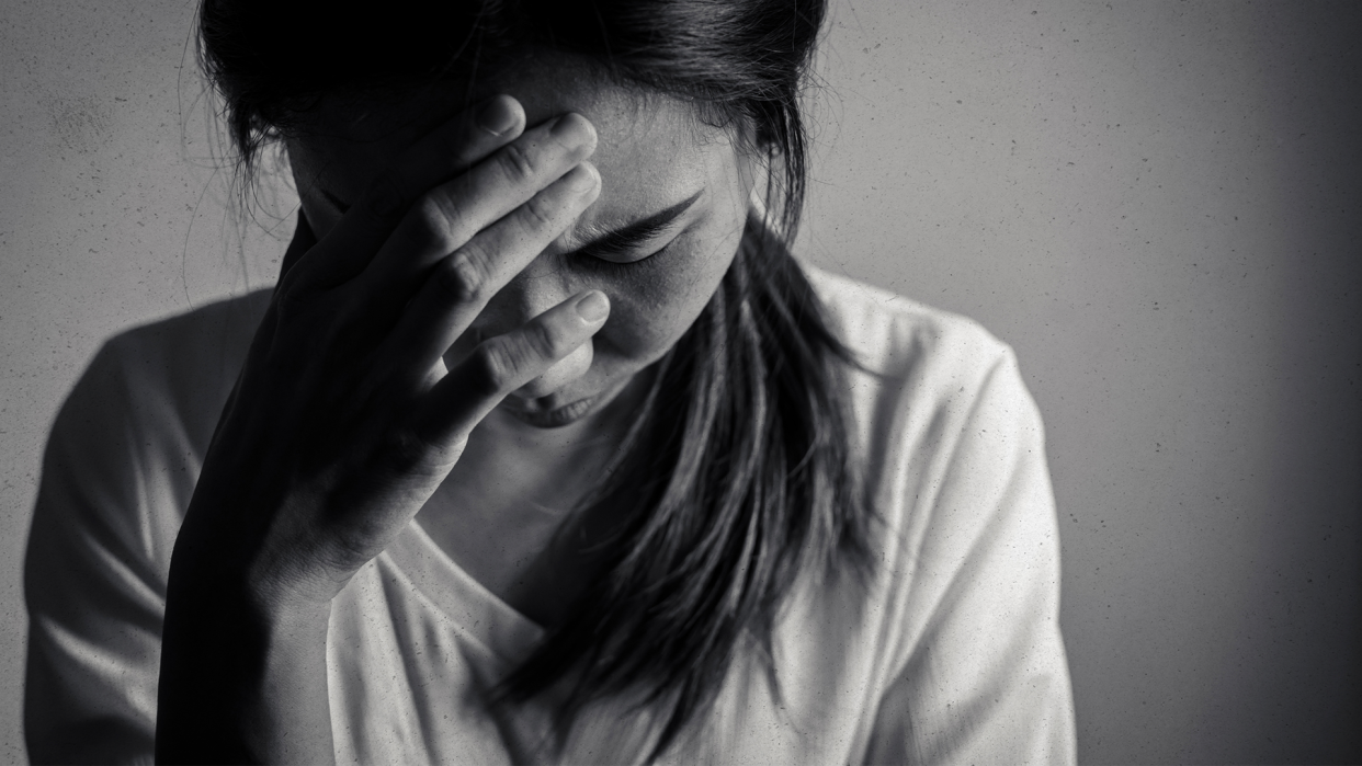 A distressed woman presses her hand to her bowed forehead.