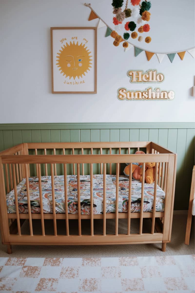 Light wood crib, green tongue and groove up half wall, hello sunshine art, tan and white checkered rug