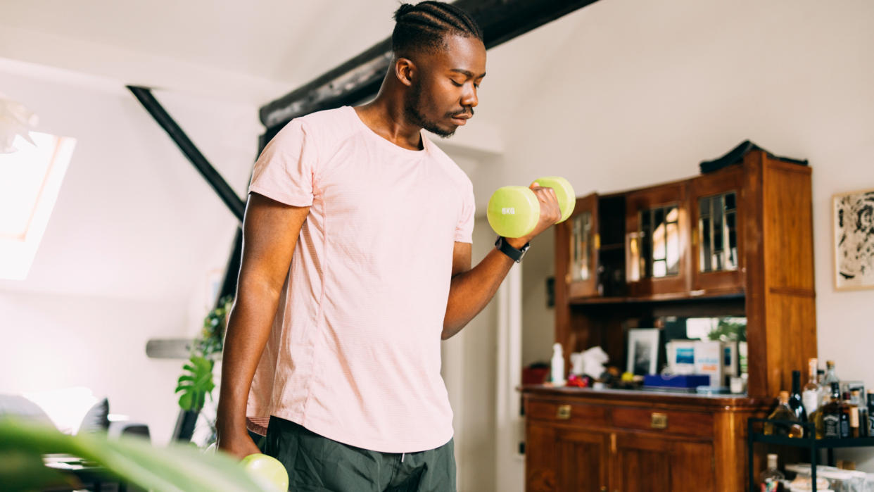  A man performing a biceps curl as part of a dumbbell workout at home . 