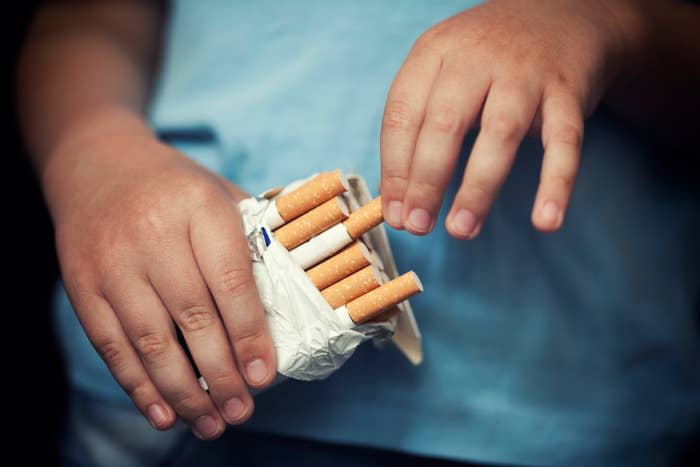 Close-up of a person's hands holding an opened pack of cigarettes, with several cigarettes partially visible inside