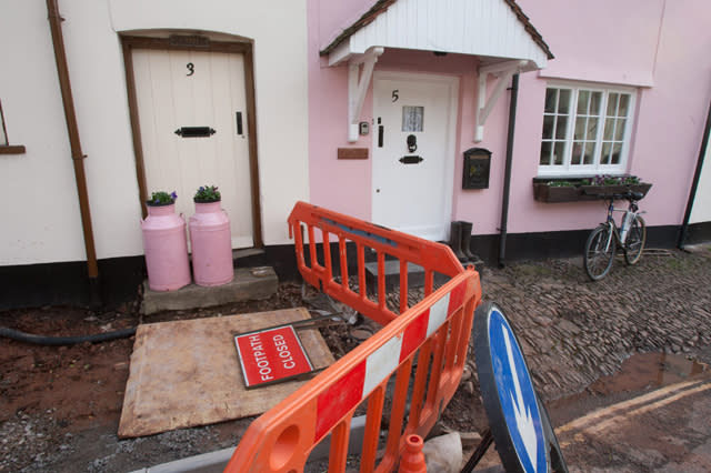 FILE PICTURE - Cobbled pathway in front of houses and businesses in West Street, Dunster. The cobbles, right, are being replaced by  brighter toned stone slabs.  Paving slabs which replaced iconic cobbles in an historic medieval village are to be removed by a cash-strapped council at a cost of ï¿½45,000 - because they are "too blue".  See SWNS story SWPAVING.  The original stones which dated back to the Bronze Age was torn from a main road in Dunster, Somerset, to improve pedestrian safety and disabled access.  The stones were replaced with blue-hued slabs, which locals complained were too blue, angular, regular, smooth and "like a path on a new housing estate".  Villagers accused the council of 'vandalism' and Historic England was furious that it was not consulted before the work began.  Now, just ten months later, the council has agreed to change the paving slabs to stones which are more in-keeping with the village - at a cost to taxpayers of ï¿½45,000.  It comes after the cash-strapped Tory approved budget cuts of ï¿½16 million earlier this year. 