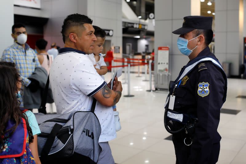 A passenger asks for information from a police officer after El Salvador's President Bukele ordered the closing of the airport in San Luis Talpa