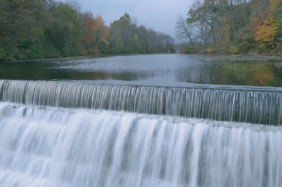 A close-up of a perfectly straight waterfall coursing down. Autumn foliage dresses up the trees behind.