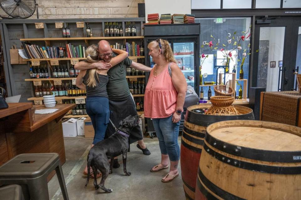 Bartender Jerome Luther hugs customer Karol King, joined by her dog Karma and Nancee Gillis, at Lucid Winery in midtown Sacramento on Wednesday, July 12, 2023. King had just donated water bowls to be spread through the warehouse space for dogs that accompany winery customers.