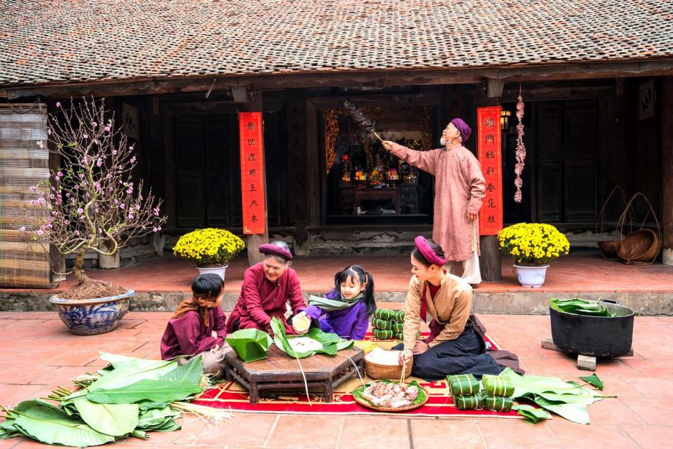 Vietnamese family members making Banh Chung together on old-styled house yard. Chung cake is a very well-known dish that could never miss on the altar, and family meal of Vietnamese during Tet holiday