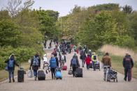 In this Saturday, May 16, 2020 photo, tourists with suitcases walk across the island of Spiekeroog, Germany. Germany's states, which determine their own coronavirus-related restrictions, have begun loosening lockdown rules to allow domestic tourists to return. (Sina Schuldt/dpa via AP)