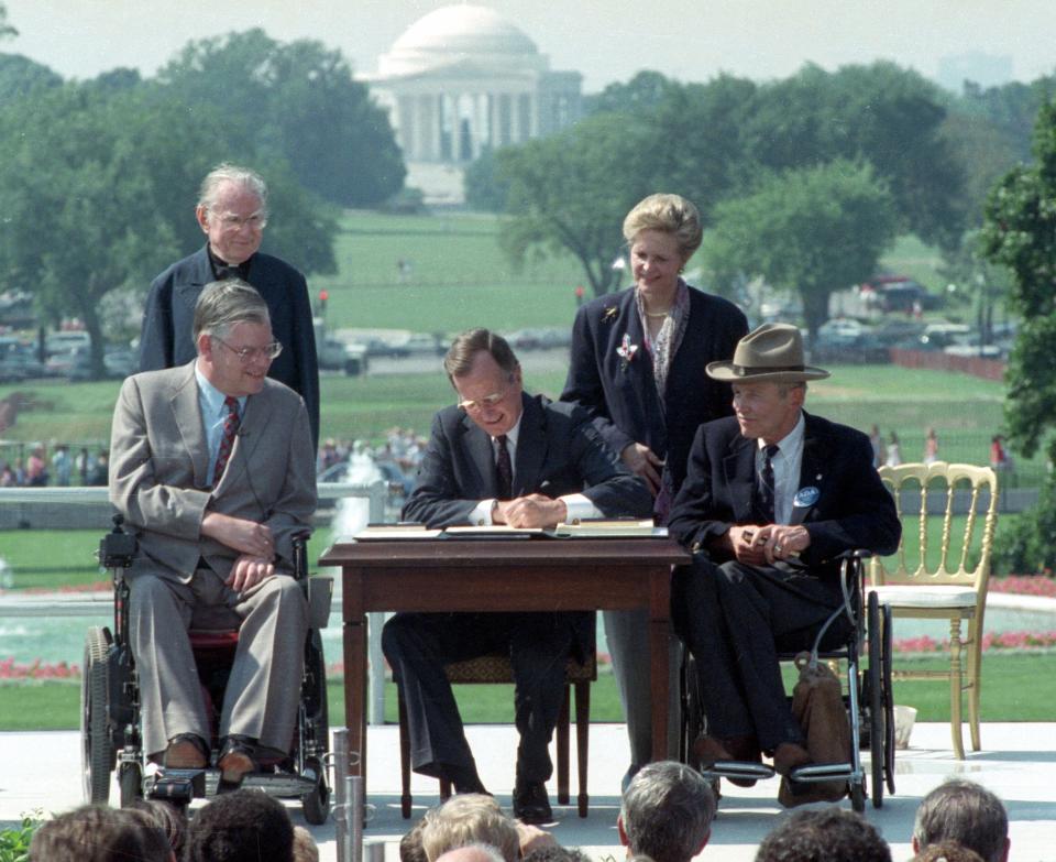 President George H. W. Bush signs the Americans with Disabilities Act during a ceremony July 26, 1990, on the South Lawn of the White House. Joining the president are, from left, Evan Kemp, chairman of the Equal Opportunity Employment Commission; the Rev. Harold Wilke; Sandra Parrino, chairman of the National Council on Disability; and Justin Dart, chairman of The President's Council on Disabilities.