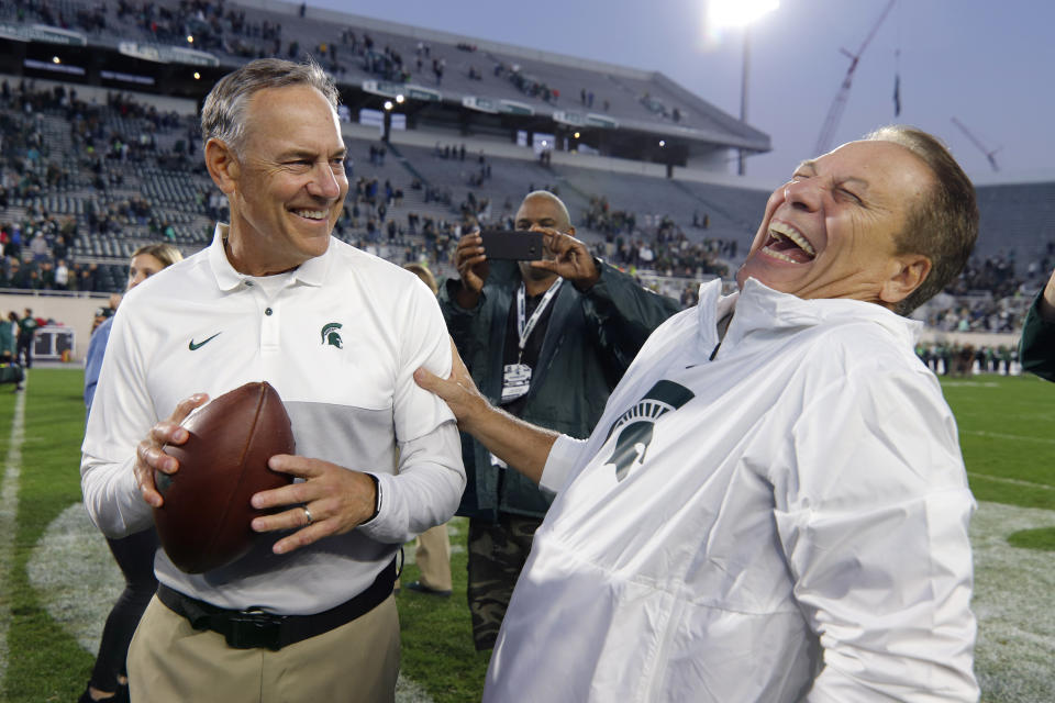 Michigan State football coach Mark Dantonio, left, and basketball coach Tom Izzo react after Dantonio was given a game ball commemorating him as the winningest football coach in Michigan State history following an NCAA college football game against Indiana, Saturday, Sept. 28, 2019, in East Lansing, Mich. (AP Photo/Al Goldis)