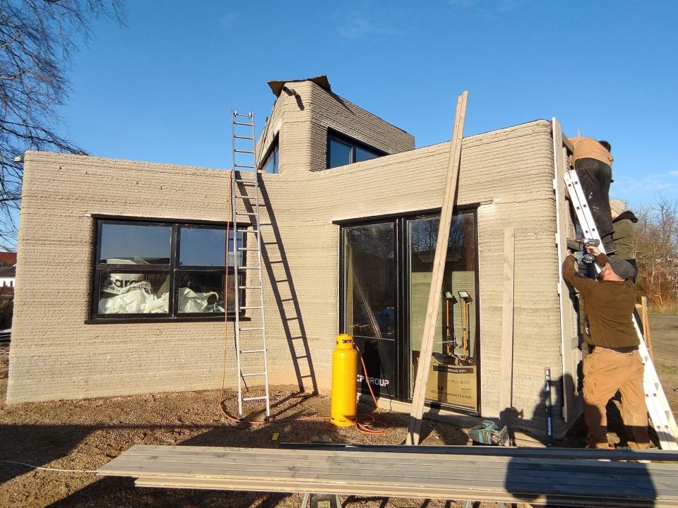 People standing next to the 3D printed tiny home with a ladder, tools.