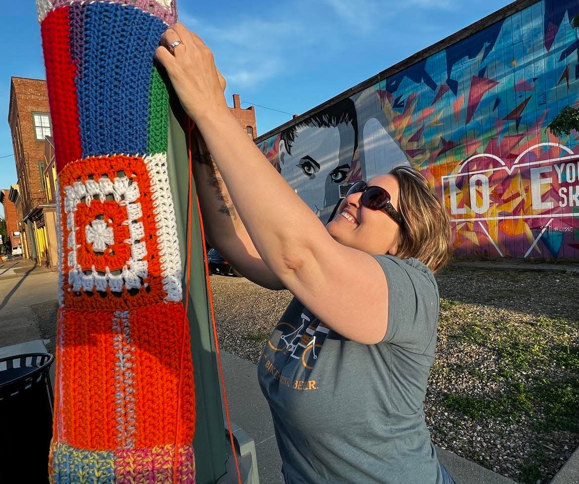 Volunteer Carla Giacobone works on yarn art on Sixth Street NW in downtown Canton. Yarn art is being installed on poles and buildings in the Sixth Street and Court Avenue NW area.