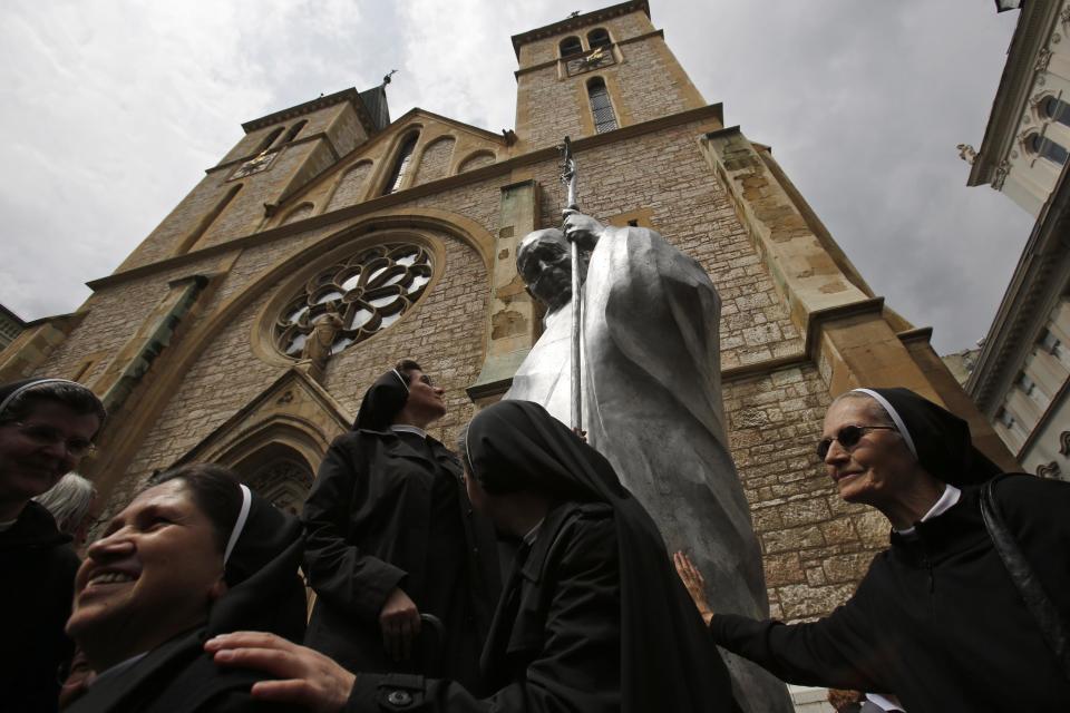 Nuns touch the statue of Pope John Paul II in front of the cathedral in Sarajevo, Bosnia, on Wednesday, April 30, 2014. Thousands of Bosnians have celebrated the canonization of Pope John Paul II by unveiling a statue in the heart of Sarajevo. John Paul’s support for Sarajevo's resistance to nationalist efforts to destroy the traditional inter-cultural and inter-religious fabric of the city during the 1992-95 war made him very popular among the city's predominantly Muslim population. The crowd shouted “long live the pope” as the three meter-high statue was unveiled Wednesday in front of the cathedral. (AP Photo/Amel Emric)