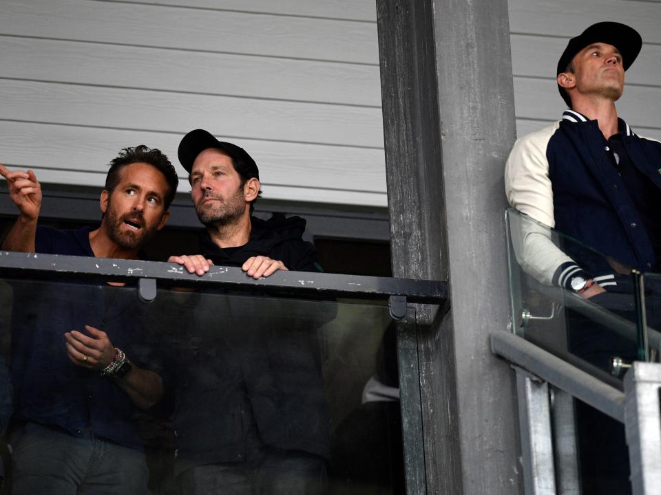 US actor and Wrexham owner Rob McElhenney (R) and US actor and Wrexham owner Ryan Reynolds (L), speaking with fellow US actor Paul Rudd (C) attend the English National League football match between Wrexham and Boreham Wood at the Racecourse Ground Stadium in Wrexham, north Wales, on April 22, 2023.