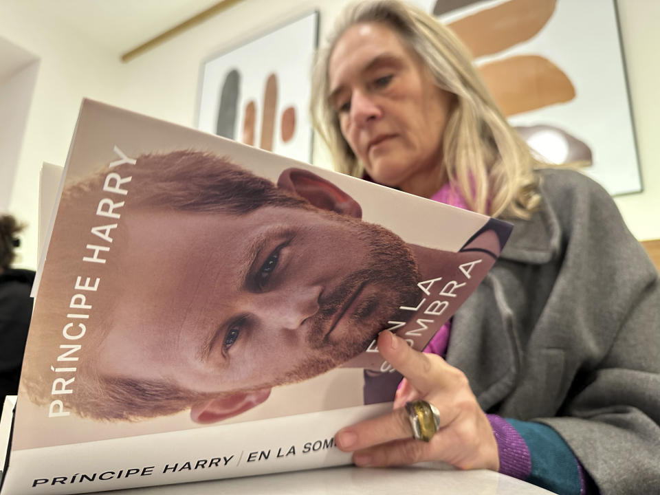A woman poses for a photo as she opens a copy of "En La Sombra" (In the Shadow), the Spanish translation of Britain's Prince Harry's memoir, "Spare," in Barcelona, Spain, Thursday Jan. 5, 2023. Prince Harry alleges in a much-anticipated new memoir, due to be published next week, that his brother Prince William lashed out and physically attacked him during a furious argument over the brothers' deteriorating relationship. (AP Photo)