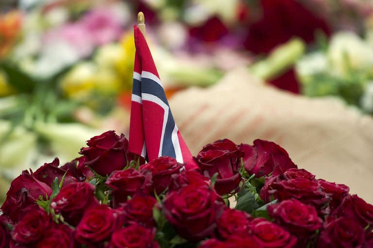 A Norwegian flag stands in a bunch of flowers during a gathering in Oslo to pay tribute to the victims. Suspected Norwegian mass killer Anders Behring Breivik faces justice Monday, after Oslo police defended the hour it took to reach the island where most of his 93 victims died in a hail of bullets