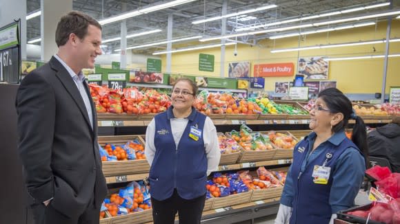 Walmart CEO Doug McMillon talking with two employees in the produce section of a Walmart store.