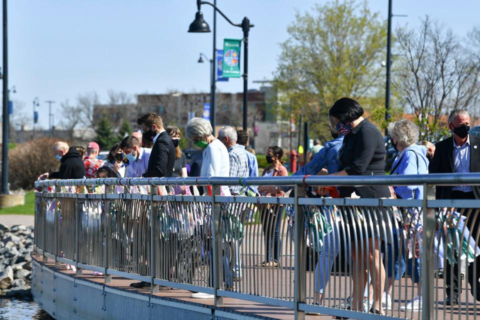 People place strips of cloth on a railing following a COVID-19 memorial event Saturday, May 1, 2021, at Lake George in St. Cloud. 