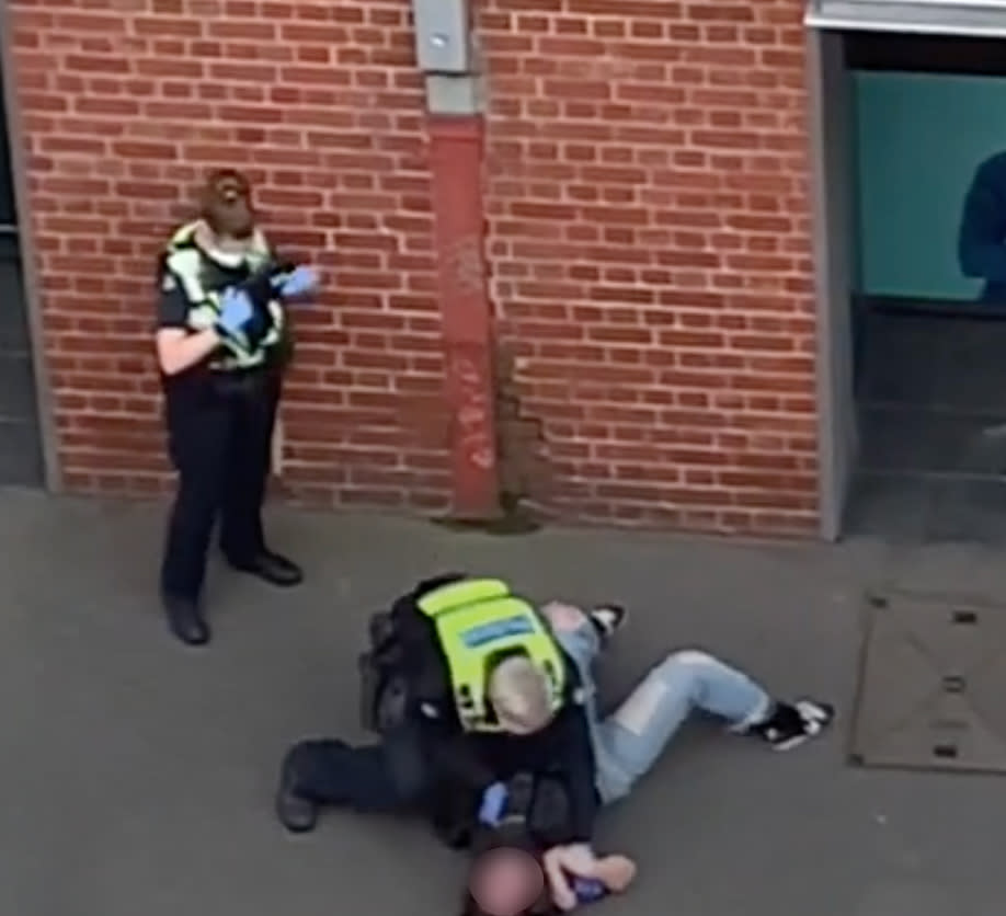 Photo shows a police officer pressing a woman into the ground.