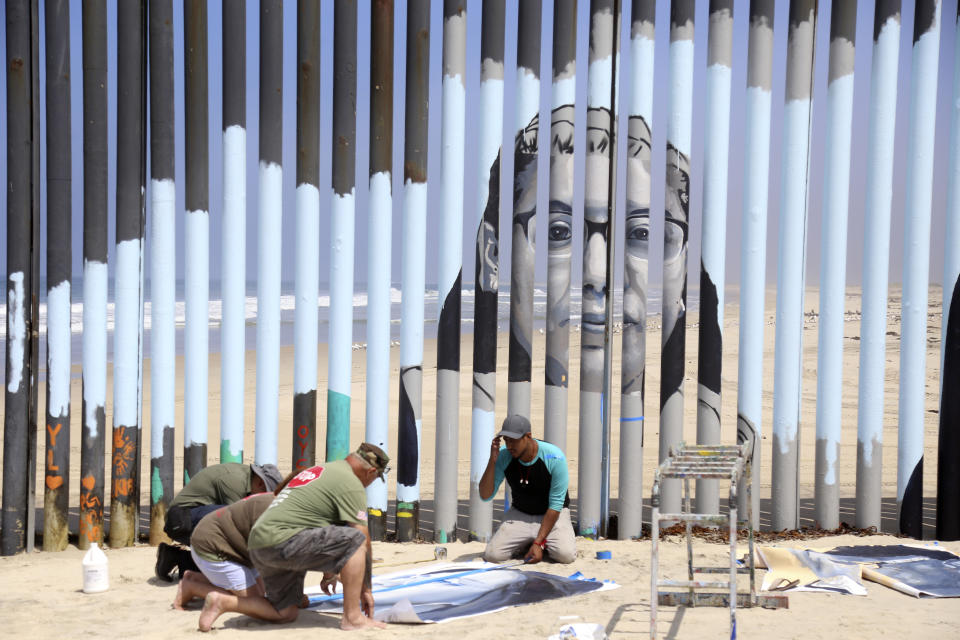 Volunteers help install a new mural on the Mexican side of a border wall that shows faces of people deported from the U.S. with barcodes that activate first-person narratives on visitors' phones, in Tijuana, Mexico, Friday, Aug. 9, 2019. Lizbeth De La Cruz Santana conceived the interactive mural Her project blends Mexico’s rich history of muralists with what can loosely be called interactive or performance art on the U.S.-Mexico border. (AP Photo/Joebeth Terriquez)