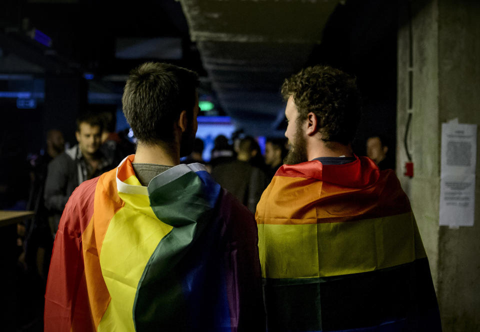 Two men draped in rainbow flags in a nightclub in Bucharest, Romania, Sunday, Oct. 7, 2018. Polls have closed in Romania after two days of voting on a constitutional amendment that would make it harder to legalize same-sex marriage. But the weekend referendum to redefine marriage failed to attract large numbers of voters and risk being voided. (AP Photo/Andreea Alexandru)