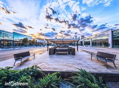 Modern and Urban Technology and Innovation Campus with outdoor employee square with benches, a wooden deck, a covered seating area, and buildings with "Infostream" logos under a cloudy sky. (CNW Group/Infostream Solutions Inc.)