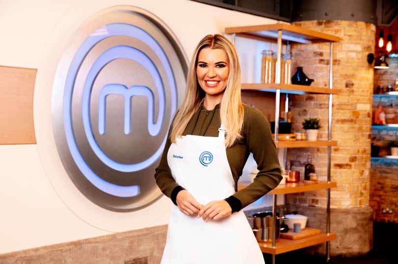 Christine McGuinness in a white apron in front of a Celebrity Masterchef logo