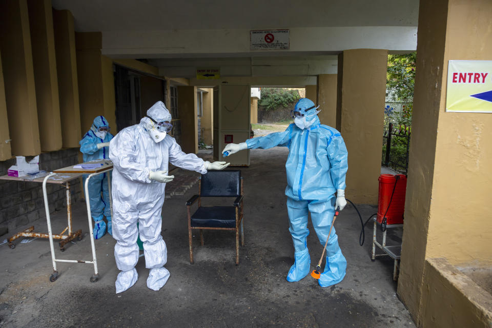 A health officer in protective suit gives hand sanitiser to another at a COVID-19 testing center in Dharmsala, India, Thursday, Oct. 29, 2020. (AP Photo/Ashwini Bhatia)