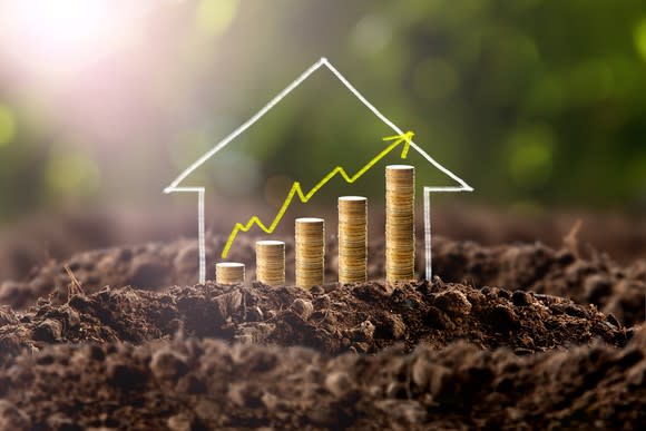 Stacks of coins rising out of the dirt, with the shape of a house drawn on top of them.