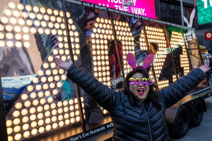 a woman with 2023 glasses and bunny ears with her arms outstretched in glee