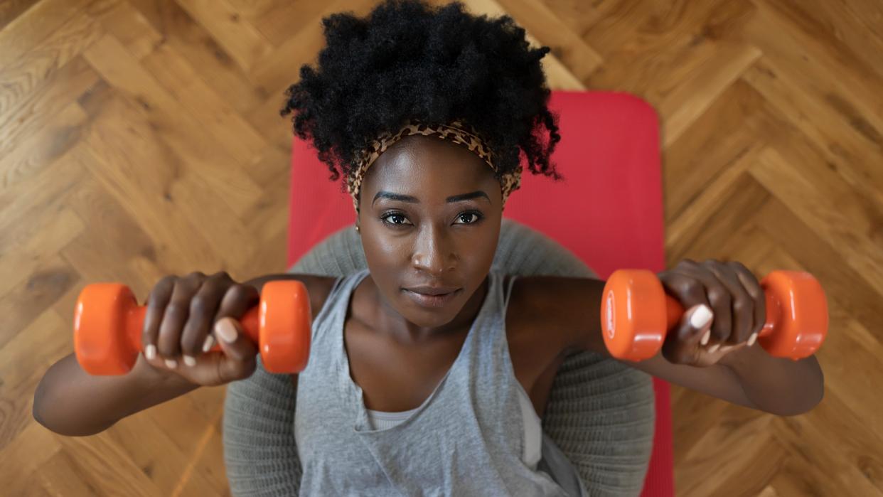  Woman doing a dumbbell chest press at home on the floor. 