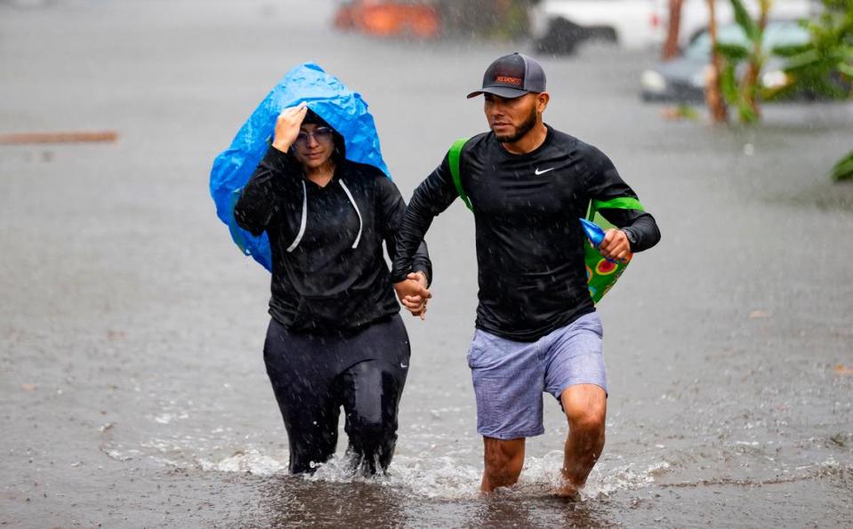 Denis Mendez, 32, left, and Isain Lopez 33, walk down a flooded street in the Edgewood neighborhood on Thursday, April 13, 2023, in Fort Lauderdale, Fla. A torrential downpour severely flooded streets partially submerging houses and cars across South Florida.