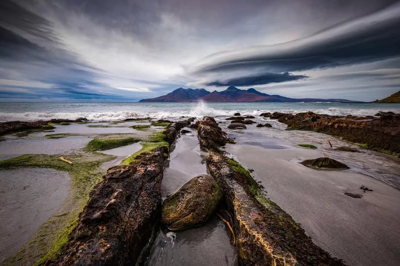 Lenticular clouds over the Isle of Rum taken from Singing Sands on the Isle of Eigg at dusk with dramatic surf. Scottish Highlands.